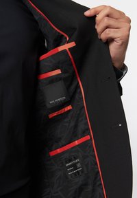 Schwarze Anzugjacke mit rotem Innenfutter. Sie verfügt über ein gemustertes Futter, mehrere Taschen und Labels für "ROY ROBSON" und "SMART FLEX."