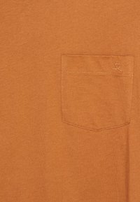 Orange bomulds t-shirt med en brystlomme prydet med en diskret hjerteformet syning. Glat tekstur med et enkelt design.