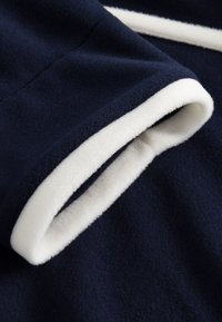 Marineblauer Fleece-Stoff mit glatter Textur, versehen mit weißem Besatz an den Bündchen. Nahaufnahme einer gerollten Kantennaht und geschichtetem Stoff.