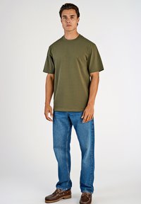 Olivgrön t-shirt med korta ärmar och rundad halsringning, ihopparad med blå denimjeans och bruna skor. Enkelt design, enfärgat, inga mönster.