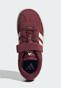 Maroon suede tenisice s bijelim trakama, podstavljenim ovratnikom i čičak trakama za sigurnu zatvorenost. Okrugli vrh i teksturirana potplat.