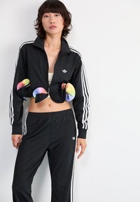 Black zip-up sports jacket with white stripes on sleeves, paired with matching black pants. Features vibrant multi-colored accents at the waist.