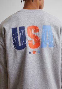 Felpa grigia con la scritta "USA" in lettere blocco blu, arancione e azzurro, con "STARTER" sotto e stelle multicolori che decorano il design.