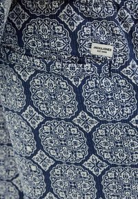 Laikku sininen kangas sisältää monimutkaisia valkoisia kukka- ja geometrisia kuvioita. Mukana on pieni etiketti, jossa lukee "JACK&JONES EST.1990." Kankaan pinta on karhea.