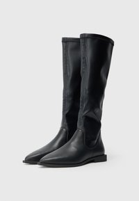Μαύρες δερμάτινες μπότες μέχρι το γόνατο με λεία υφή, μυτερή μύτη και μινιμαλιστικό σχεδιασμό, με αντίθετη ραφή και επίπεδη σόλα.