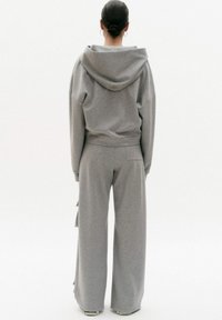 Grijze katoenen hoodie met een grote capuchon, ruime pasvorm, gecombineerd met wijde grijze sweatpants met rimpelaccenten aan de zijkant.