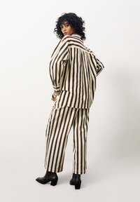 Gestreepte katoenen shirt- en broekenset in crème en bruin, met brede verticale strepen, een relaxte pasvorm en zwarte blokhak-schoenen.