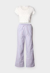 Haut blanc court à manches courtes avec de petites impressions de papillons violets, associé à un pantalon large lilas à rayures verticales bleues et blanches.