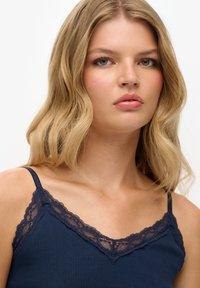 Camisola a costine navy con delicata rifinitura in pizzo navy lungo il collo e le spalline, caratterizzata da un design aderente e una morbida texture.