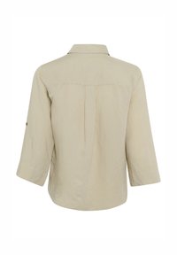 Camicia a maniche lunghe di un beige chiaro con colletto, pieghe sul retro e polsini con bottoni. Realizzata in un tessuto testurizzato.