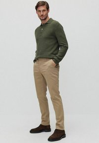 Grön stickad pikétröja kombinerad med beige byxor och bruna mockastövlar. Outfiten har en åtsittande design och subtila texturer.