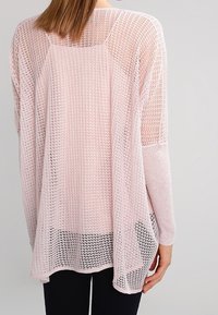 Hellrosa, locker gestrickter Pullover mit langen Ärmeln und entspannter Passform. Die Struktur ist ein offenes Maschenmuster, das Atmungsaktivität ermöglicht.