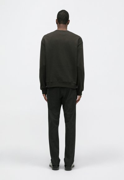 Ciemnobrązowa bluza z okrągłym dekoltem, z ribbowanymi mankietami i dołem. W połączeniu z antracytowymi spodniami. Prosty design; brak widocznych logo lub wzorów.