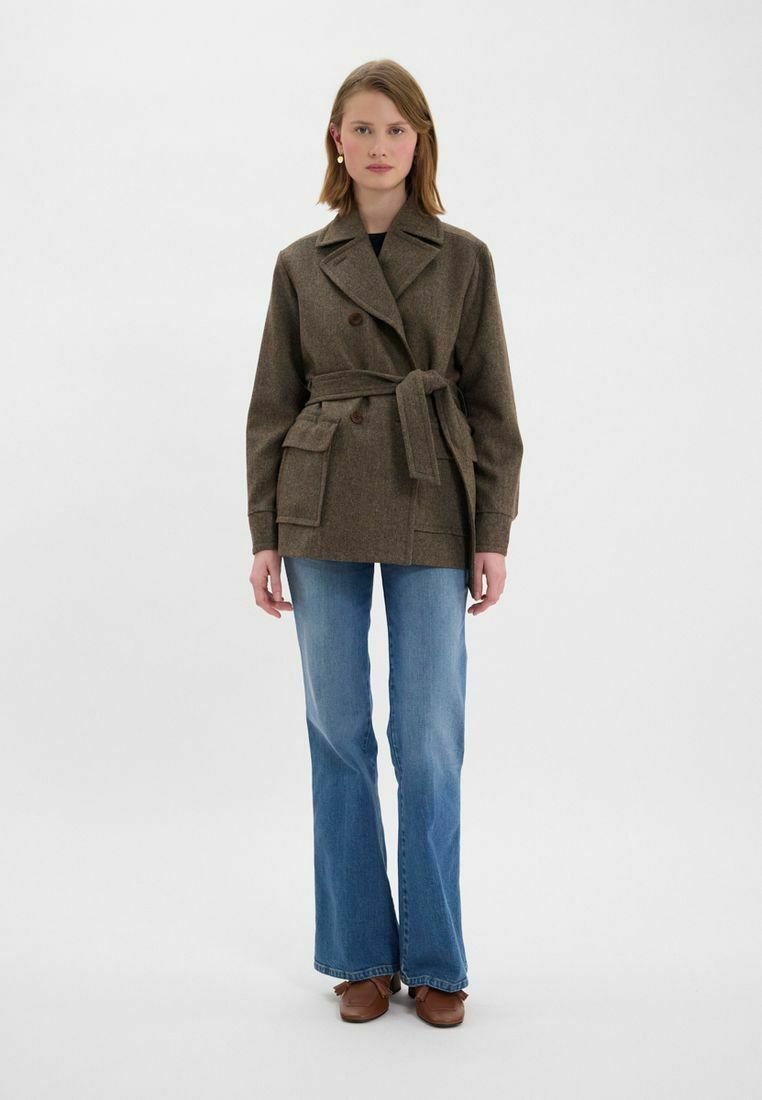 Peacoat en mélange de laine marron avec une ceinture à nouer, design double boutonnage, poches latérales et larges revers, associé à un jean évasé et des chaussures marron.