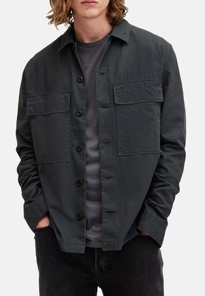 Mørkegrå button-up jakke med to brystlommer, let materiale, subtil struktur og en afslappet pasform over en grå t-shirt.