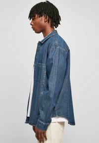 Denim jakas vidēji zilā krāsā, relaksēta piegriezuma ar punktotu apkakli, vienu krūšu kabatu un garām piedurknēm ar pogājamiem kultūriem.