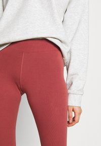 Burgundifärgade leggings i elastisk tyg, med en mjuk textur och sömlös design, kombinerade med en ljusgrå sweatshirt.
