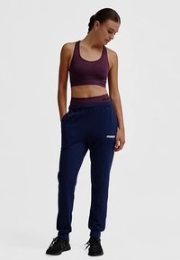 Sportbeha in donkerpaars met een ronde hals en dunne bandjes, gecombineerd met marineblauwe joggers met een trekkoord en logodetail.