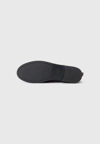 Semelle de chaussure noire avec un motif de semelle minimal, marquée "BOSS" et taille "35" sur un fond blanc uni.