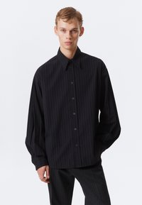 Mustavalkoraidallinen nappitakkipaita, jossa on terävä kaulus, pitkät hihat ja rento istuvuus. Valmistettu kevyestä kankaasta, jossa on sileä pinta.