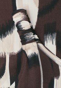 Cordon noué sur un tissu marron et beige avec un motif abstrait de coups de pinceau noirs et blancs.