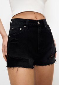 Shorts in denim nero con vita alta, caratterizzati da dettagli strappati, orli sfilacciati e bottoni argentati sulle tasche frontali.