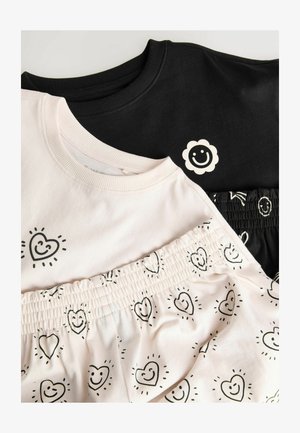 Dve mikiny: jedna čierna s bielym logom usmievavého kvetu, druhá svetloružová s čiernymi vzormi srdca. K nim patrí pár kraťasov s podobným dizajnom.