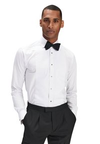 Valkoinen paita, jossa on laskostettu etuosa ja musta rusettisolmio. Mustat suorat housut, joissa on taskut. Raikas ja muodollinen ilme.
