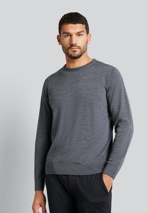 Grauer Pullover mit langen Ärmeln aus glattem Strickgewebe und runder Ausschnitt. Gerippte Bündchen und Saum. Trägt dunkle Hosen.
