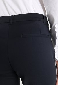 Granatowe spodnie o gładkiej fakturze, z tylną kieszenią i dopasowanym designem w talii. Materiał wydaje się lekki i elastyczny.