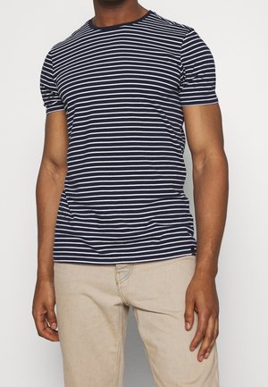 Marineblau-weiß gestreames T-Shirt mit kurzen Ärmeln in taillierter Form und Rundhalsausschnitt. Glatte Stofftextur, kombiniert mit beigen Hosen.