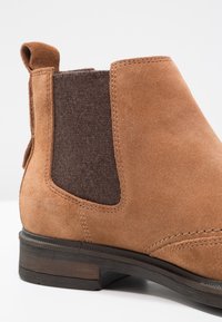Botte Chelsea en daim fauve avec panneau latéral élastique foncé et petit talon en bois empilé, vue rapprochée de côté.