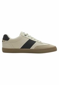 Basket beige avec une bande noire et des accents en daim texturé beige. Présente des lacets blancs, une semelle en caoutchouc plate et un col rembourré.