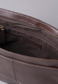 Brown leather bag with a smooth texture, featuring a zippered compartment and a stitched edge. Inner lining is darker fabric, with a brand label visible.