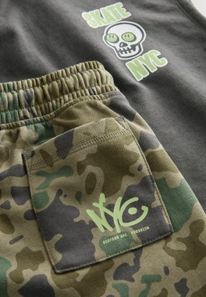 Canottiera grigia con grafica verde "SKATE NYC" e teschio. Pantaloni corti con motivo camouflage e vita elastica, etichetta del logo NYC verde.