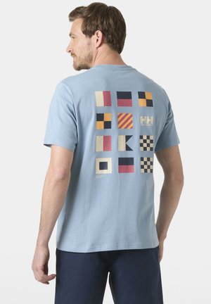 Hombre con camiseta azul claro con 12 banderas náuticas de colores y el logo "HH Helly Hansen" en la parte trasera.