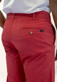 Rote Baumwollhose mit geradem Schnitt, ausgestattet mit einer Gesäßtasche mit Knopfverschluss und einem kleinen Markenschild. Glatte Textur.