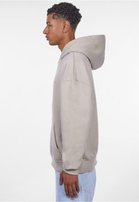 Hellgrau Hoodie mit großer Kapuze, gerippten Bündchen, Fronttasche und gesticktem Text. Glatte Textur und entspannter Schnitt.