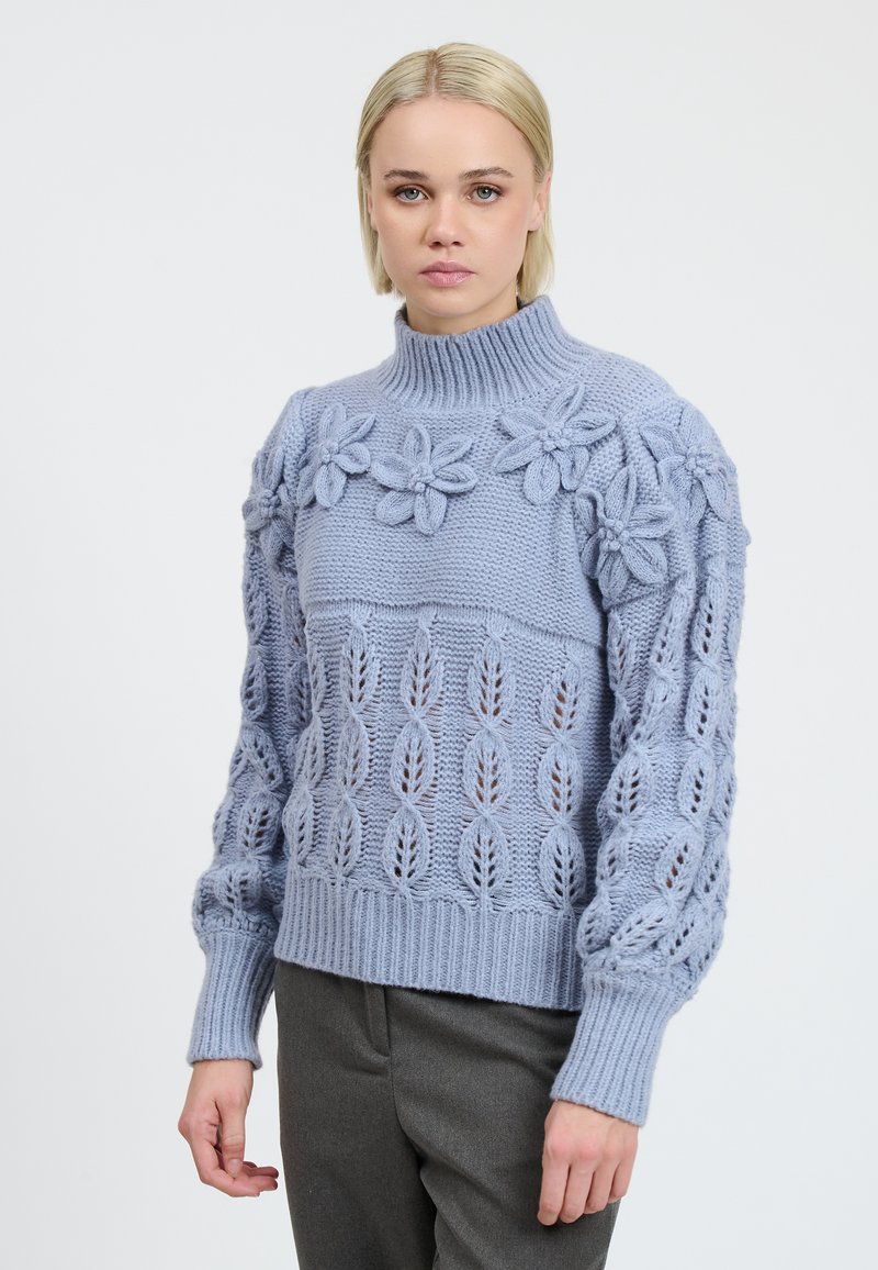 Hellblauer Strickpullover mit floralen Akzenten, langen Ärmeln, gerippten Bündchen und einem hohen Kragen mit einem strukturierten Blattmuster.