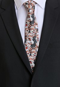 Krawat w wzory przedstawiający rysunkowe renifery w odcieniach bieli, pomarańczy i czerni, na ciemnym tle, noszony z czarnym garniturem.