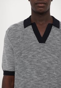 Polo shirt grigio a maglia con finitura testurizzata, caratterizzato da un colletto blu scuro e maniche corte, che presenta un design a V.