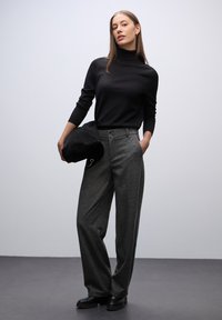 Zwarte coltrui, grijze wijde broek met knoopaccenten, en zwarte handtas, op een model tegen een neutrale achtergrond.