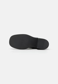 Suola di scarpa nera con una texture liscia e un leggero motivo. Punta arrotondata e tacco basso. Realizzata in materiale durevole. Design minimalista.