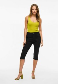 Musta capri farkut, jotka ovat slim fit -mallia, yhdistettynä ribattyyn limenvihreään hihattomaan puseroon. Mallilla on päällään vihreät, lohkarekorkoiset sandaalit, joissa on ketjureuna.