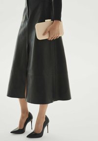 Juoda odinė sijonas su plyšiu, derinamas su juodais smailiais aukštakulniais ir smėlio spalvos rankinėle. Dizainas pasižymi švariomis linijomis ir lygiu paviršiumi.