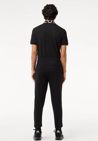 Zwarte sportieve jumpsuit met korte mouwen, voorzien van een bedrukte kraag, elastische taille en taps toelopende broekspijpen; ontworpen voor comfort en bewegingsvrijheid.