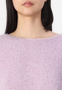 Pulover tricotat de culoare mov deschis, cu guler larg și rotund. Textura este moale și ușor pufoasă, evidențiind cusături libere și vizibile.