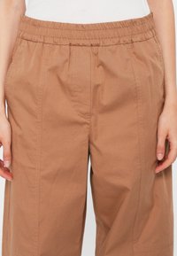 Brązowe, lekkie spodnie z elastycznym pasem, charakteryzujące się prostymi nogawkami, kieszeniami bocznymi oraz subtelną fakturą z przeszyciami.