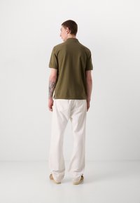 Olivengrøn polo T-shirt med korte ærmer, båret med hvide løstsiddende bukser. Har en klassisk krave og et enkelt design.