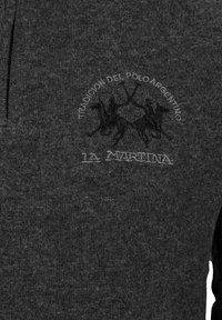 Mörkgrå tröja gjord av strukturerad tyg, med en broderad logotyp med hästmän och texten "Tradicion del Polo Argentino" och "La Martina."